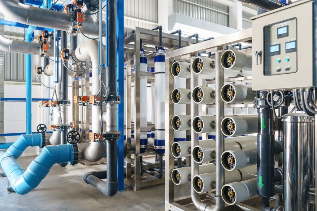Interior view of an industrial water filtration facility featuring reverse osmosis membrane units, stainless steel piping, control valves, and monitoring panel within a clean, high-tech environment.